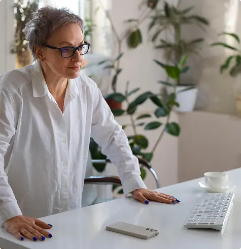 An adult woman standing at a desk, illustrating a quick return to work and light daily activities following Shoulder Artery Embolization (SAE) treatment.