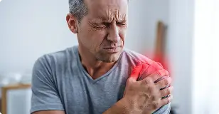 A man wincing in pain while holding his shoulder, illustrating Shoulder Artery Embolization (SAE) for relief from frozen shoulder and inflammation.